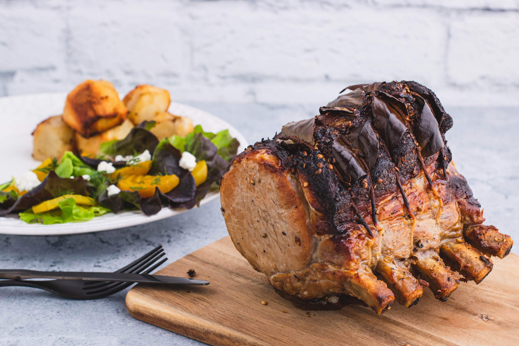 A whole roasted pork rib sits beside a dinner plate full of sliced pork, potatoes, and salad.