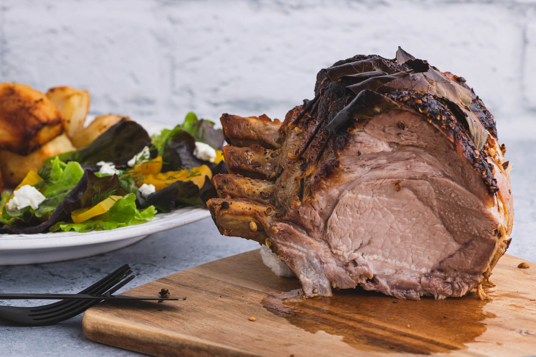 A pork rib roast with a slice taken out sits beside a dinner plate full of sliced pork, potatoes, and salad.