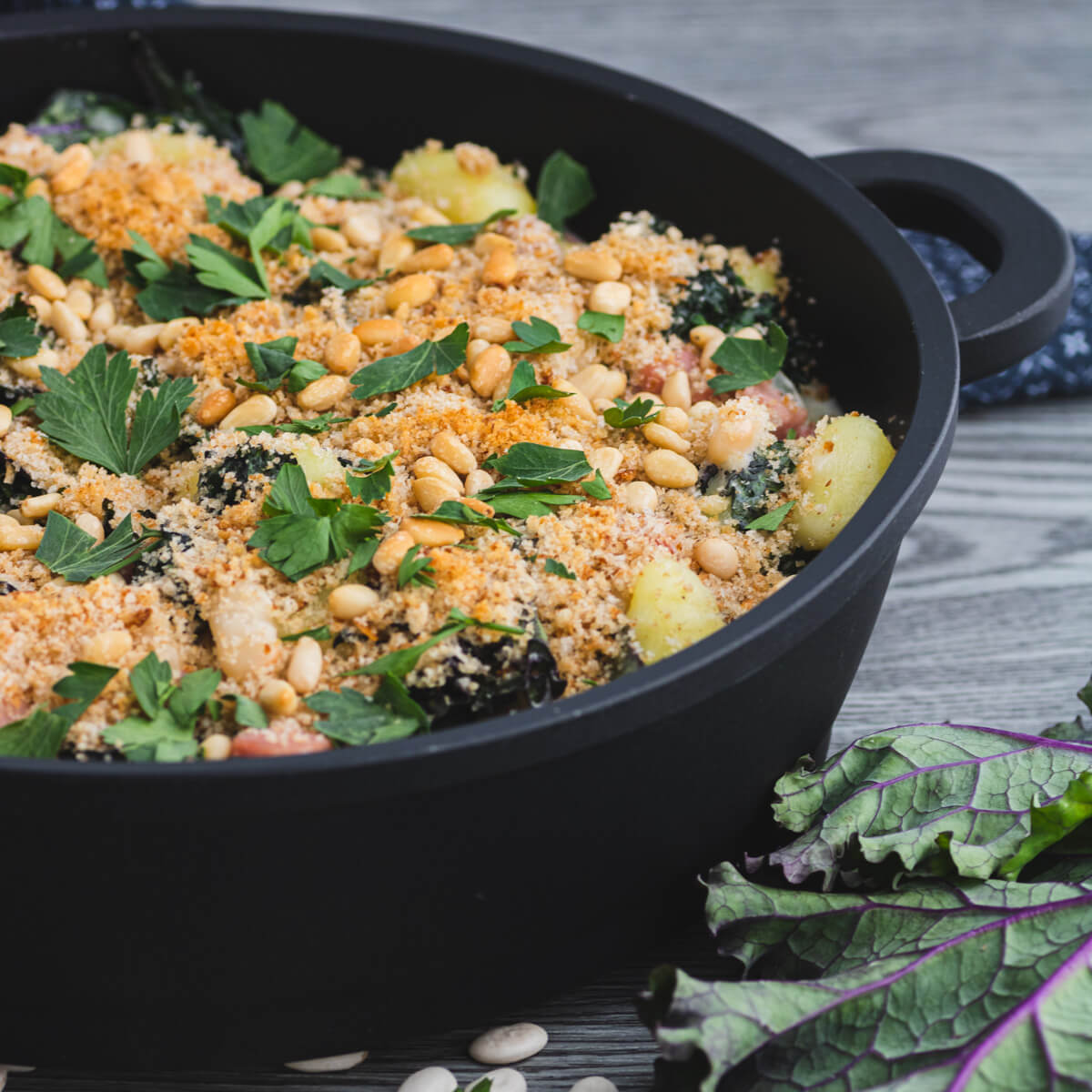 A baking dish full of Creamed Kale Gnocchi full of ham and beans in a creamy sauce topped with golden breadcrumbs and pine nuts.