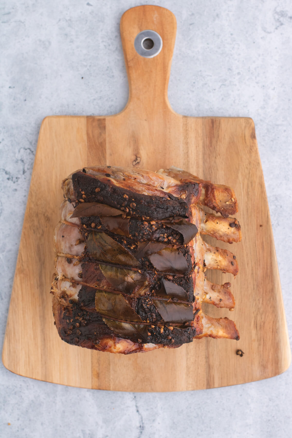 A whole roasted pork rib roast on a wooden cutting board.