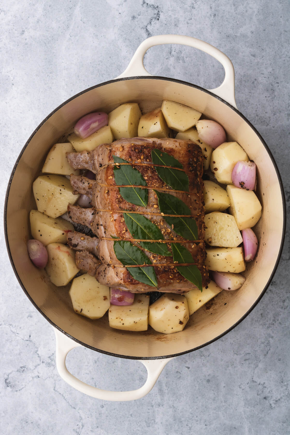 A browned pork rib roast nestled among potatoes and onions in a Dutch oven.