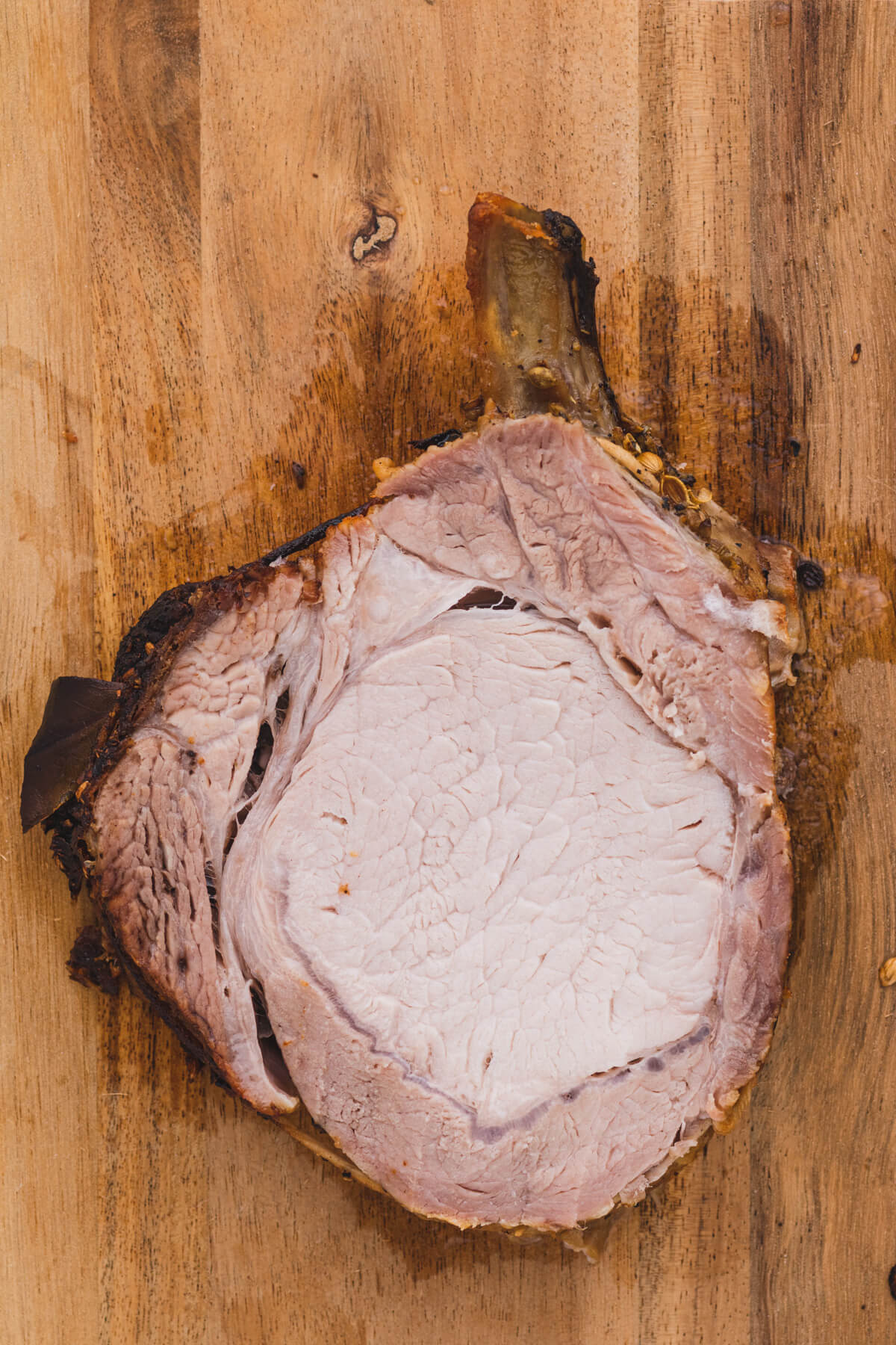 One slice of brined pork rib roast on a wooden cutting board.