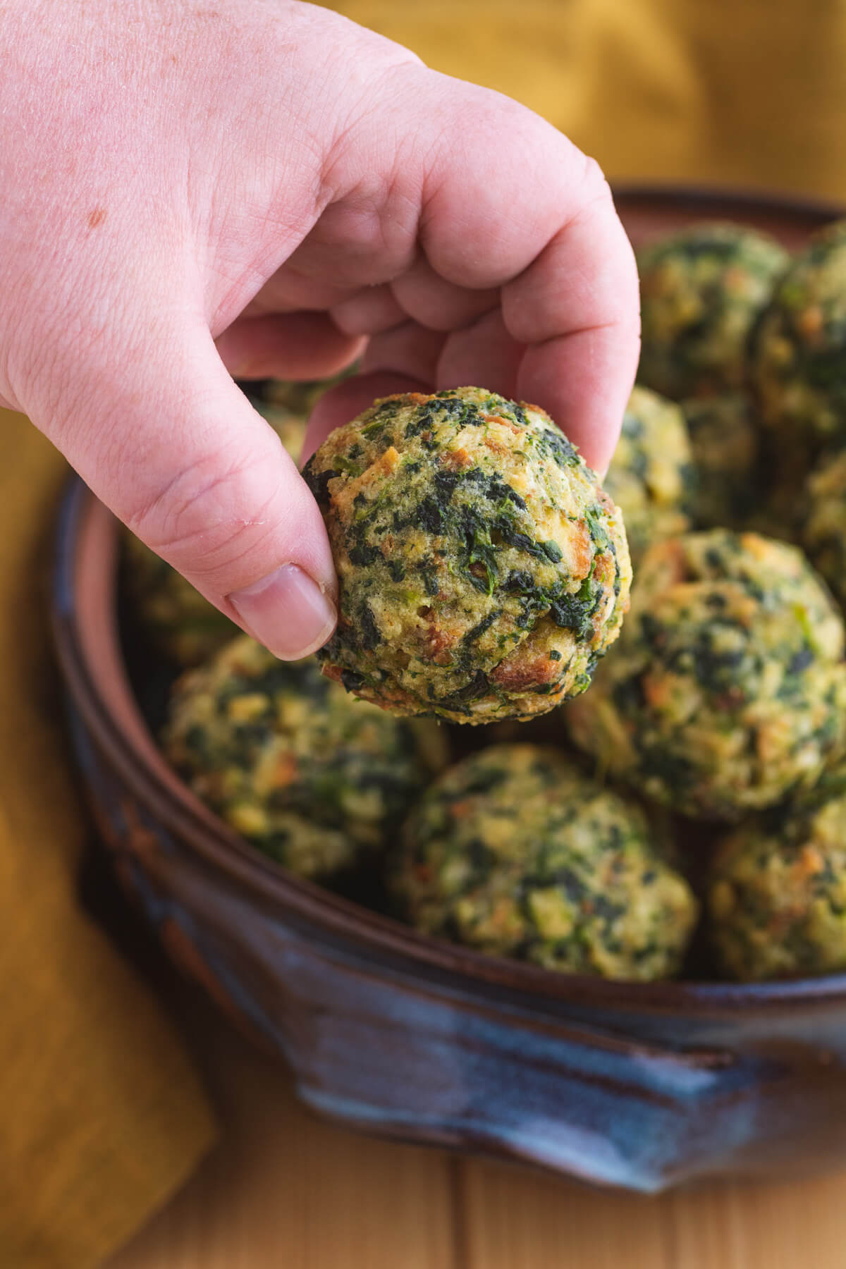 A hand grabbing a spinach stuffing ball out of a casserole dish.