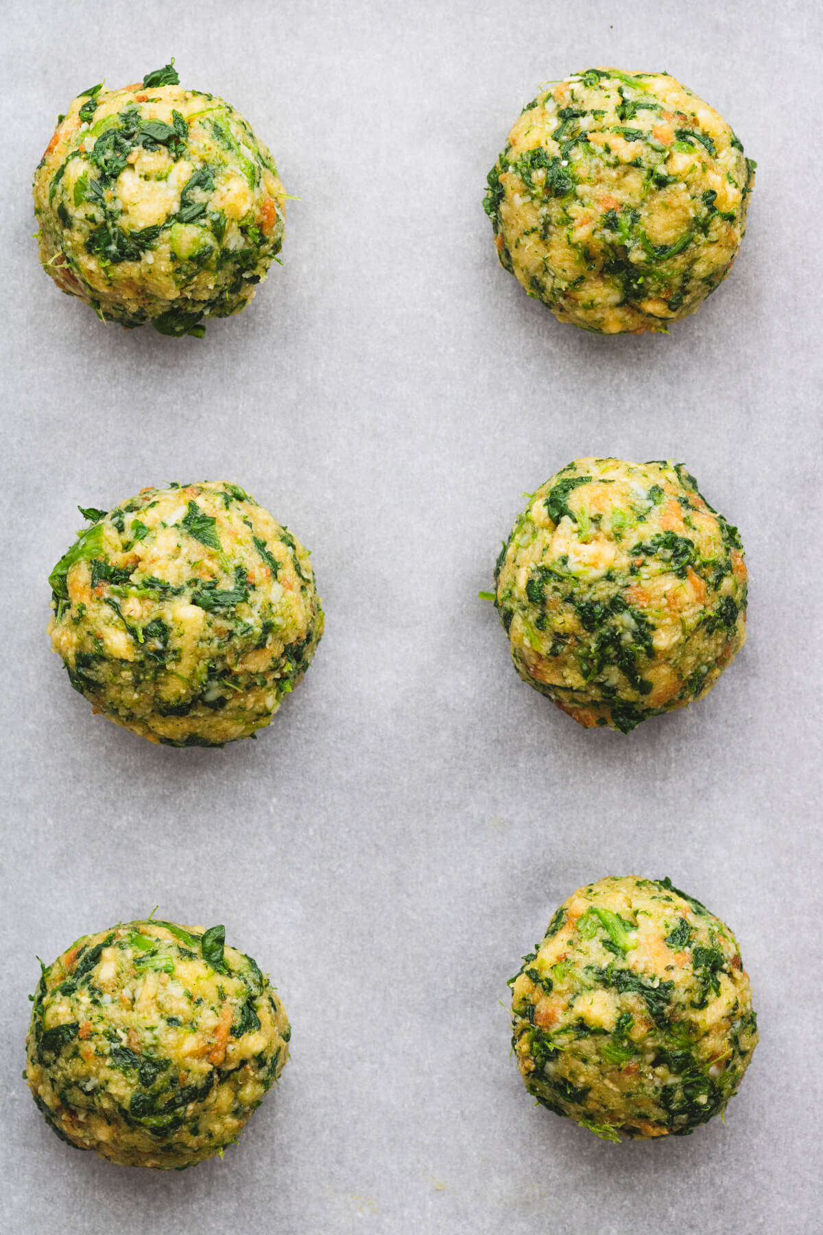 Spinach stuffing balls lined up on a piece of parchment paper.