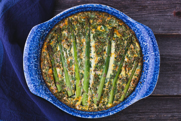 A baked Asparagus Quiche in a blue ceramic baking dish.