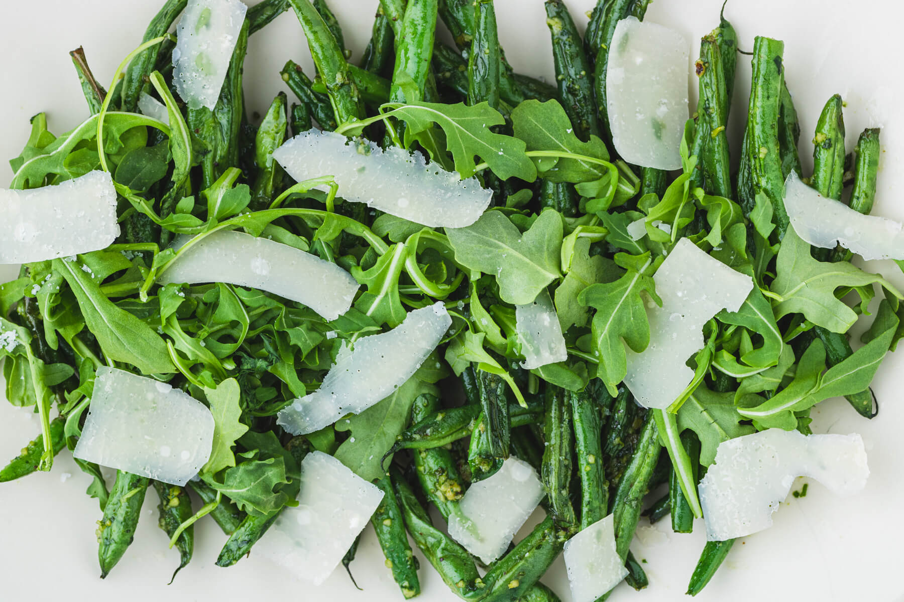 Vibrant green Air Fryer Pesto Green Beans with Pesto on a white platter topped with baby arugula and Parmesan cheese.
