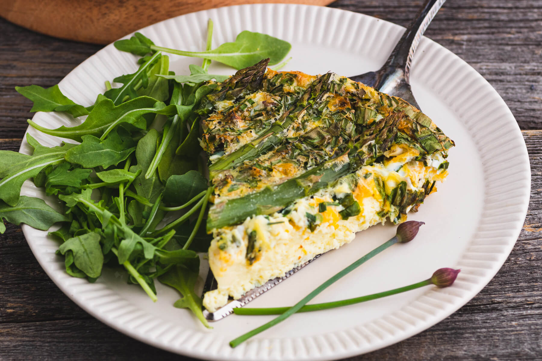 A silver pie server under a slice of Asparagus quiche with wild ramps on a white plate.