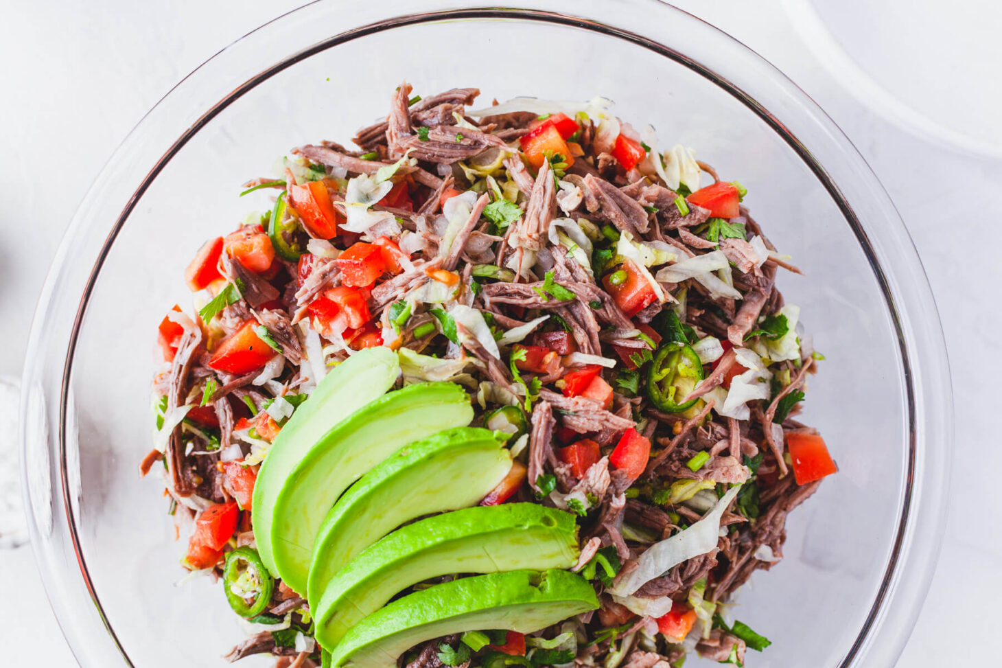 A glass bowl filled with brightly coloured Salpicón (Mexican Shredded Meat Salad) topped with sliced avocado.
