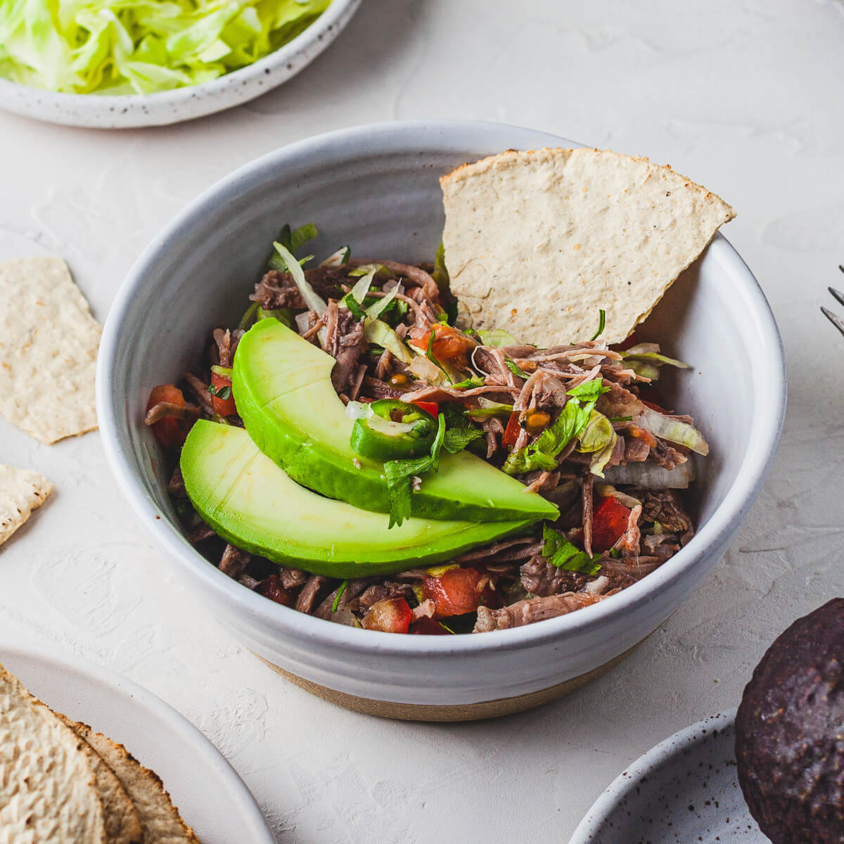 A white bowl filled with brightly coloured Salpicón (Mexican Shredded Meat Salad) topped with sliced avocado.
