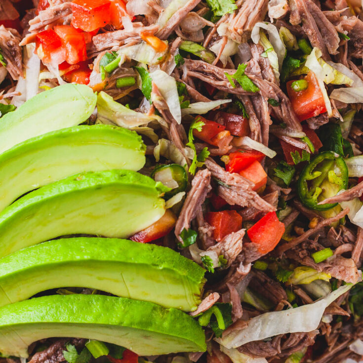 Brightly coloured Salpicón (Mexican Shredded Meat Salad) topped with sliced avocado.
