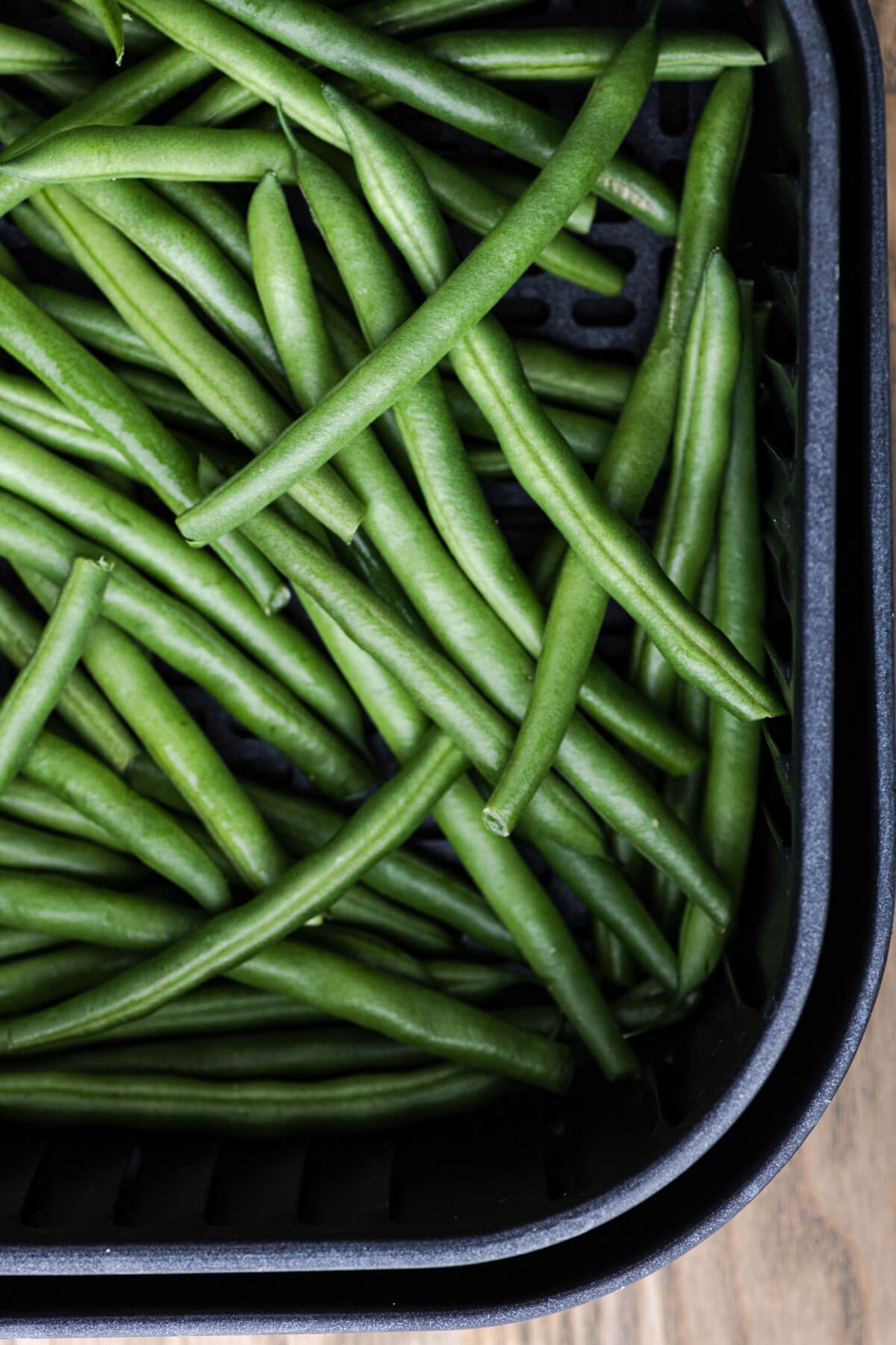 Vibrant raw green beans in an air fryer basket.