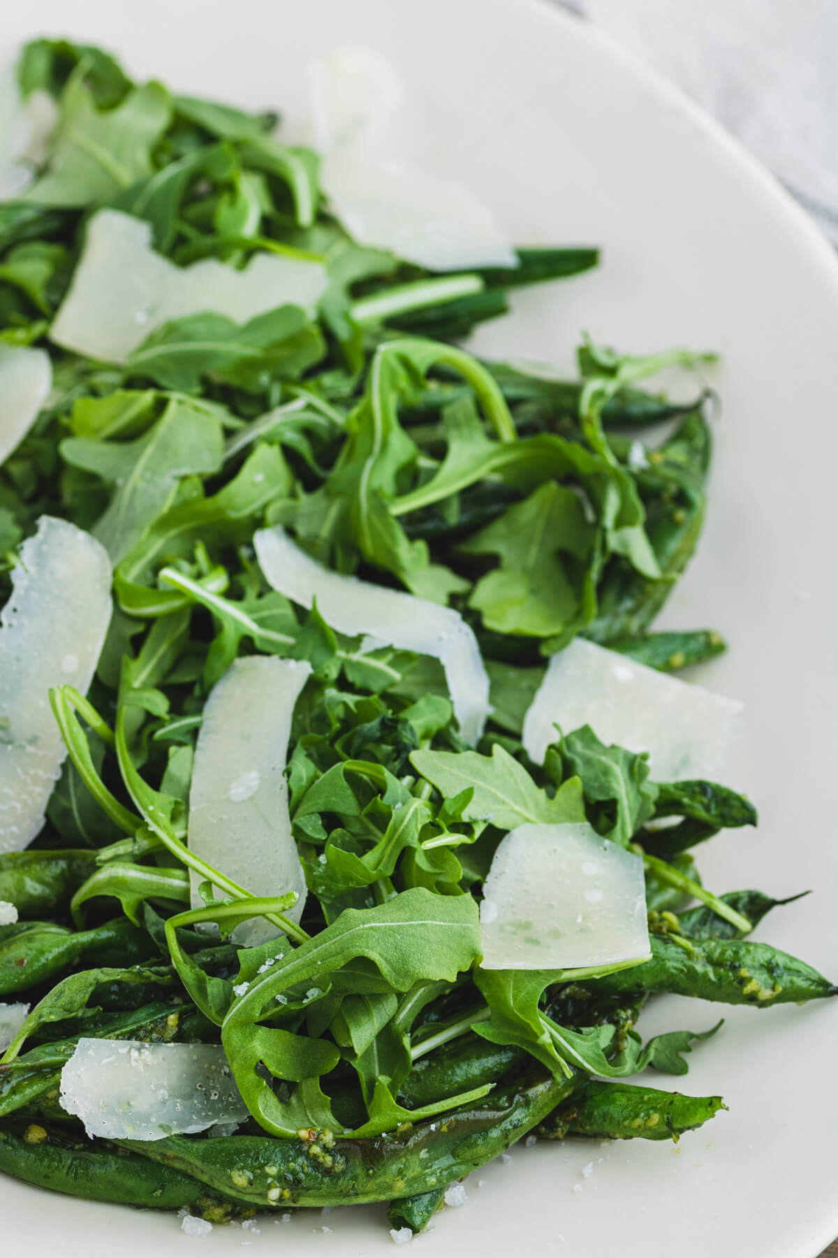 Vibrant green Air Fryer Green Beans with Pesto on a white platter topped with baby arugula and Parmesan cheese.