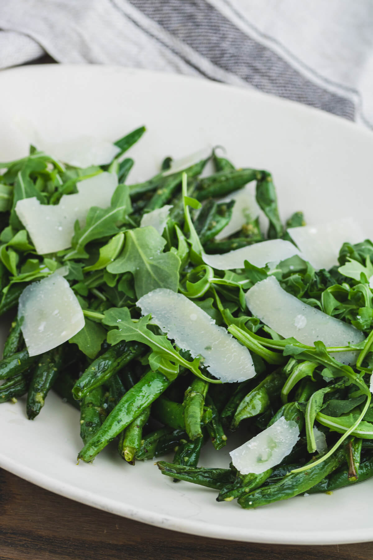 Vibrant green Air Fryer Green Beans with Pesto on a white platter topped with baby arugula and Parmesan cheese.