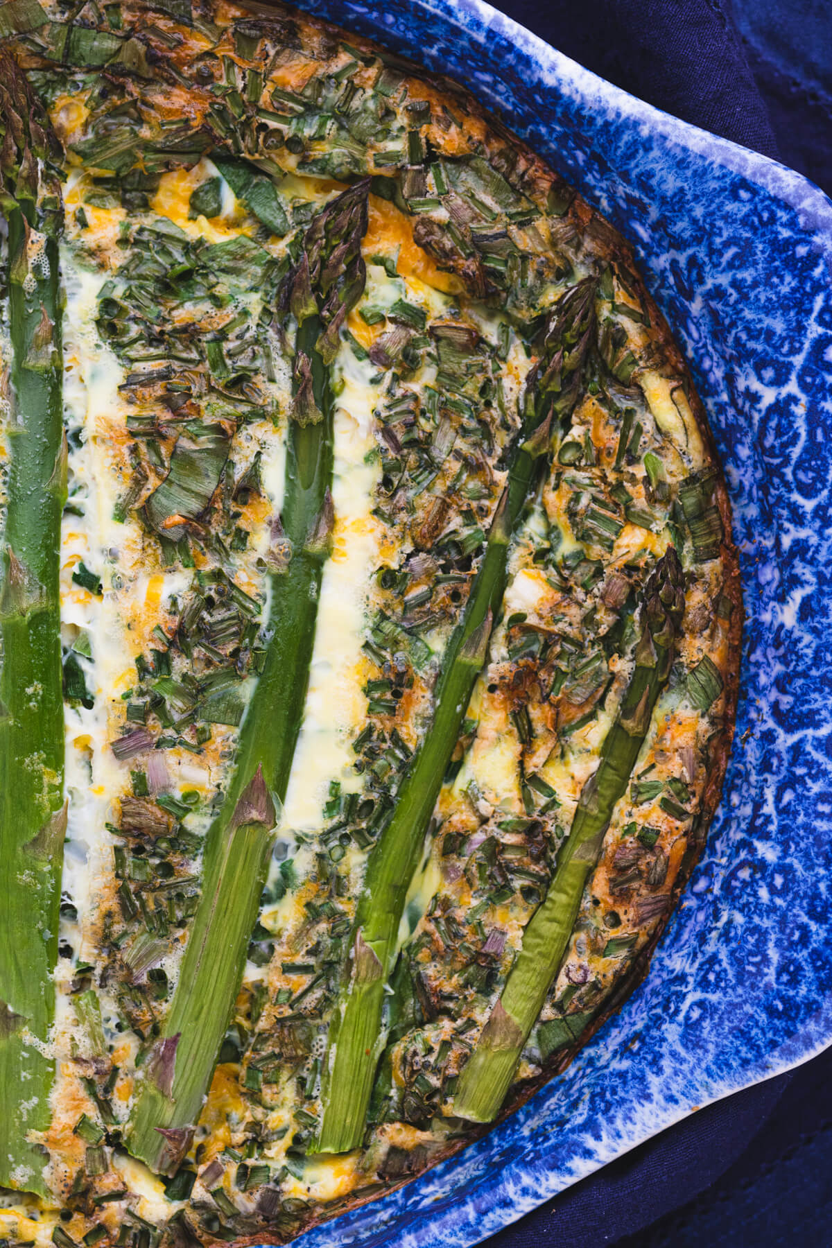 A baked Asparagus Quiche in a blue ceramic baking dish.