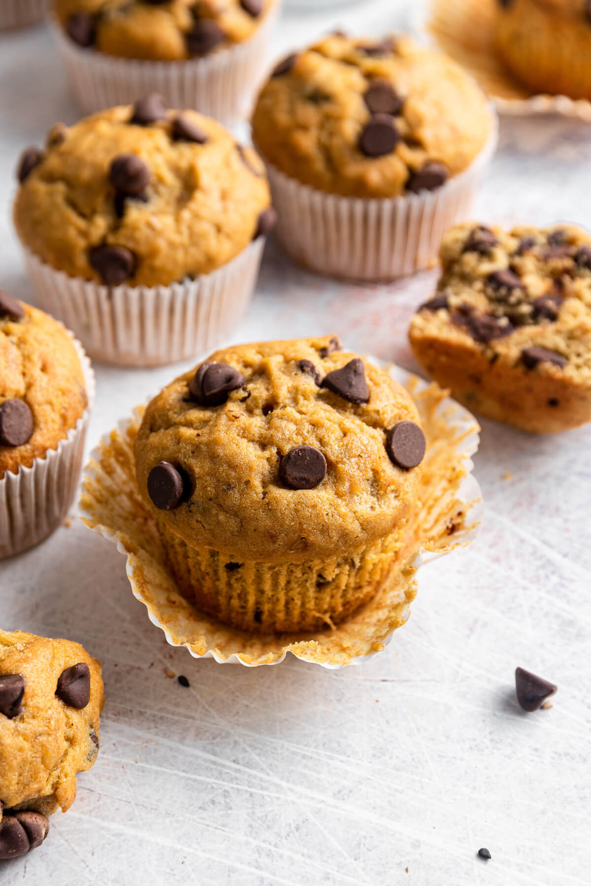 A golden baked Tahini Chocolate Chip Banana Muffin with loose muffin paper.