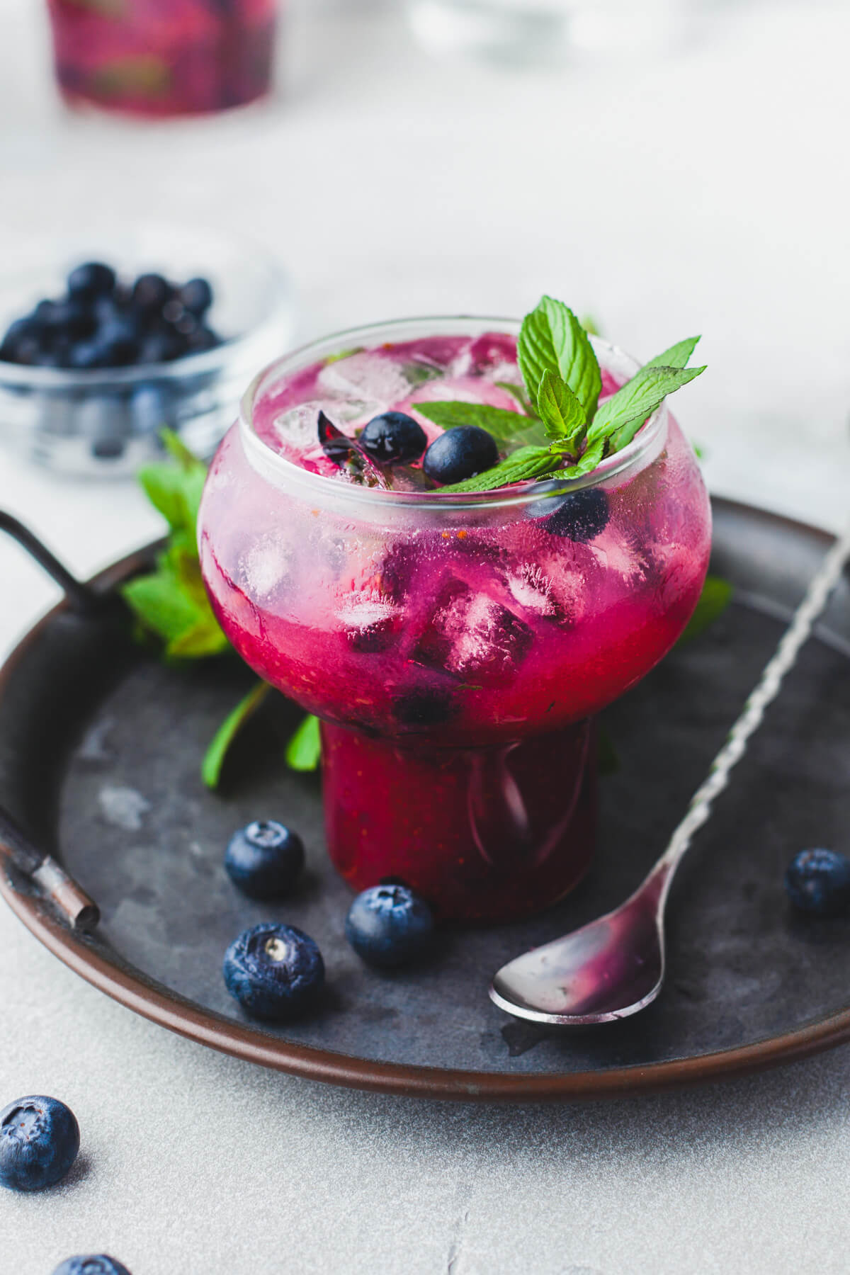 A vibrant purple Blueberry Mojito Cocktail garnished with fresh mint sits on a dark metal tray.