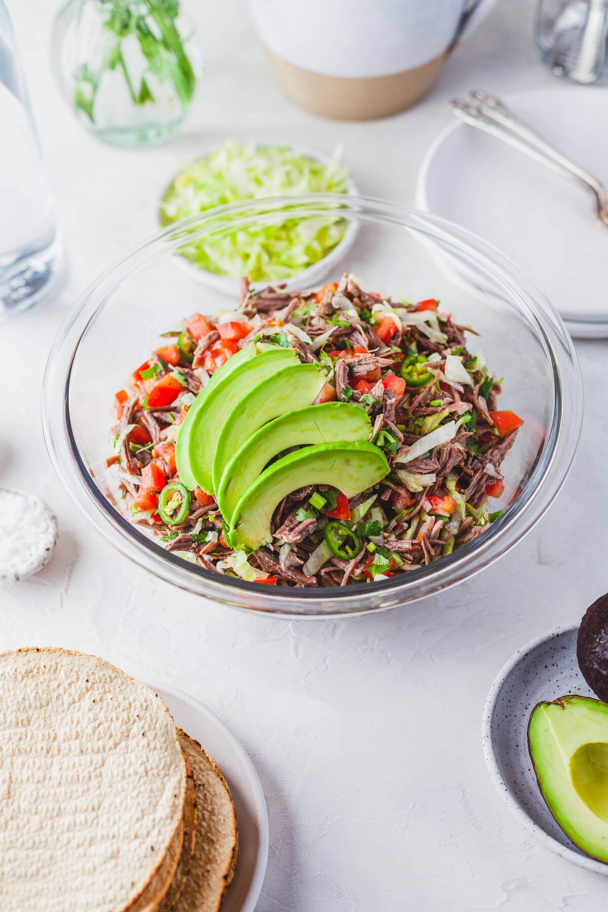 A glass bowl filled with brightly coloured Salpicón (Mexican Shredded Meat Salad) topped with sliced avocado.