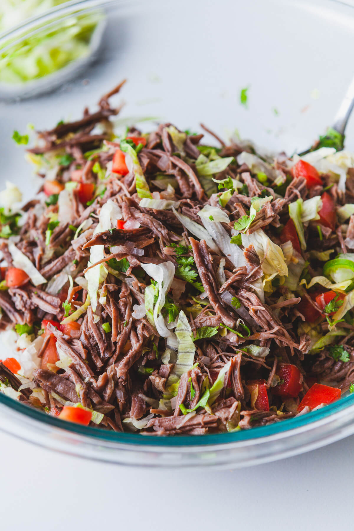 A glass bowl filled with brightly coloured Salpicón (Mexican Shredded Meat Salad).