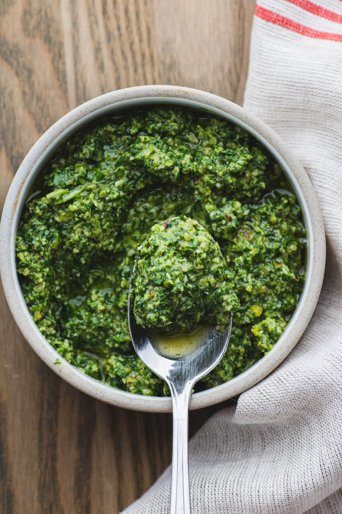 A spoon holds a portion of pesto above a small stoneware bowl filled with vibrant green arugula pesto.