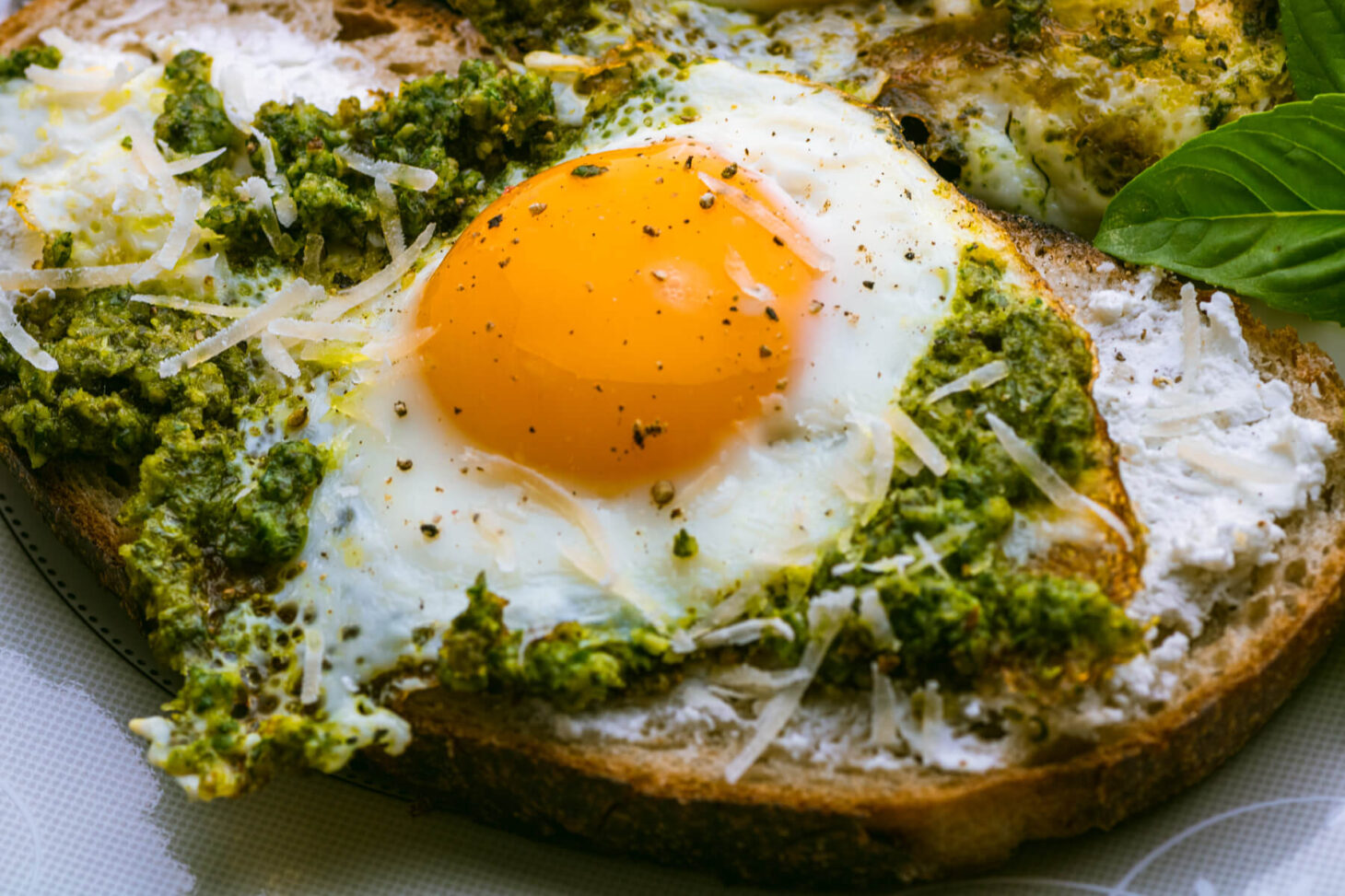 A fried Pesto Egg on toast with sunny side up yellow egg yolk and vibrant green basil pesto.