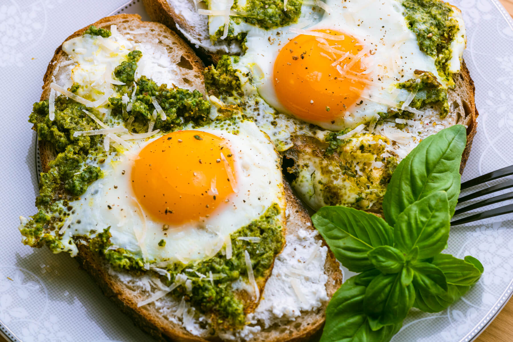 A plate of two fried Pesto Eggs on toast with sunny side up yellow egg yolks and vibrant green basil pesto.