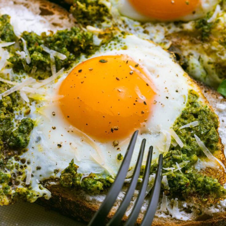 A fried Pesto Egg on toast with sunny side up yellow egg yolk and vibrant green basil pesto.