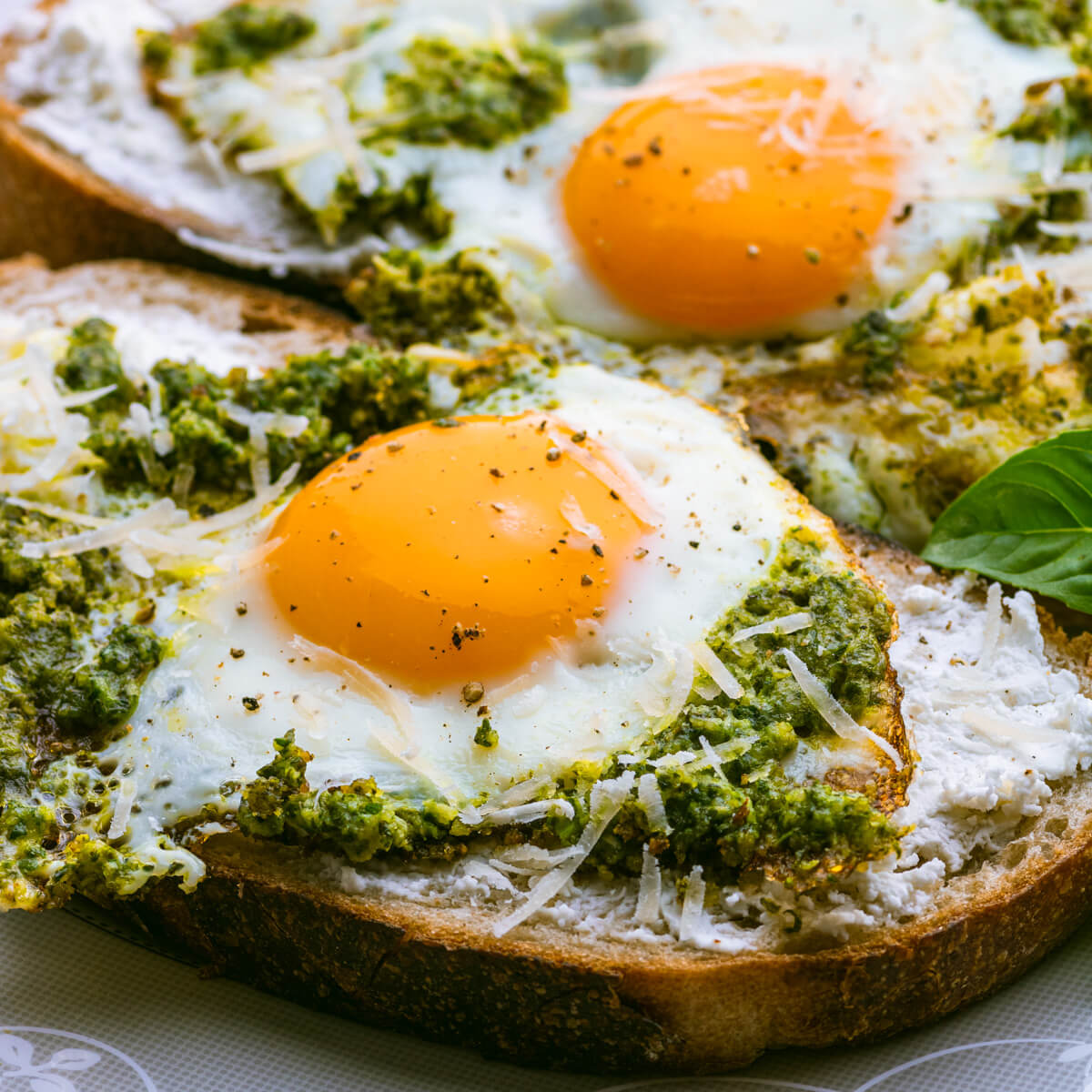 Two fried Pesto Eggs on toast with sunny side up yellow egg yolks and vibrant green basil pesto.