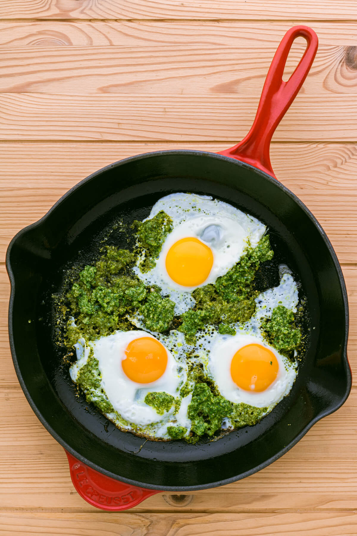 Three sunny side up Pesto Eggs in a red le Creuset skillet.