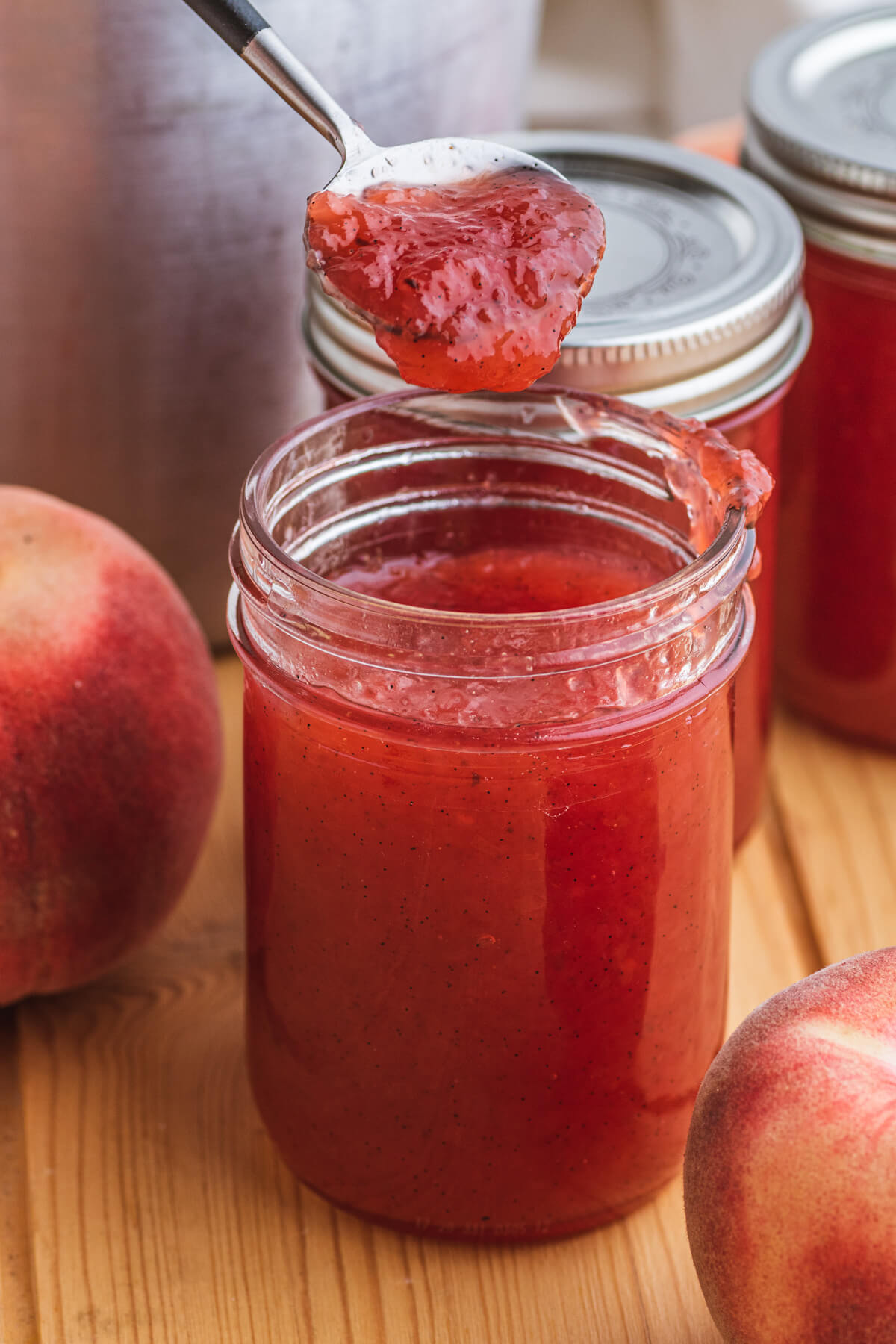 A jar full of pink hued White Peach Jam with a spoonful of jam over top. 
