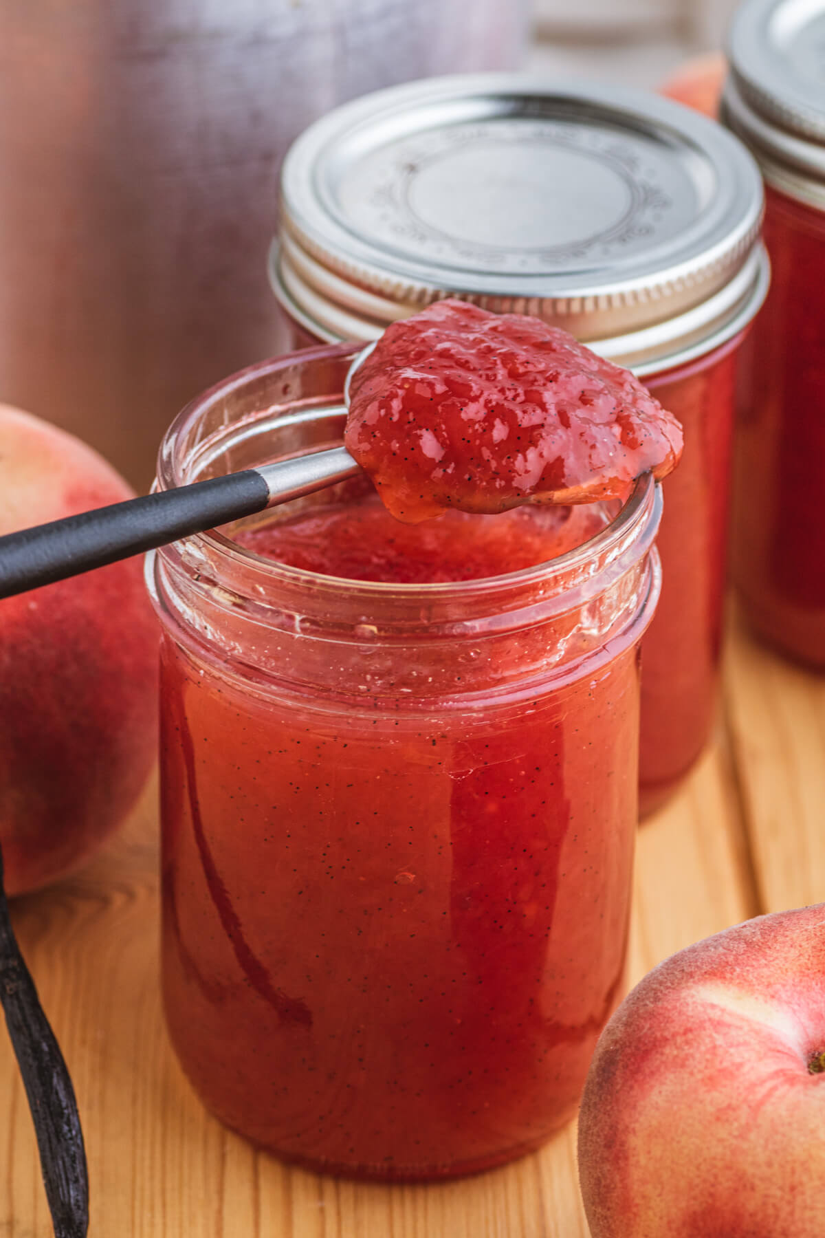 Close up of a spoon full of White Peach Jam over a jar of jam.
