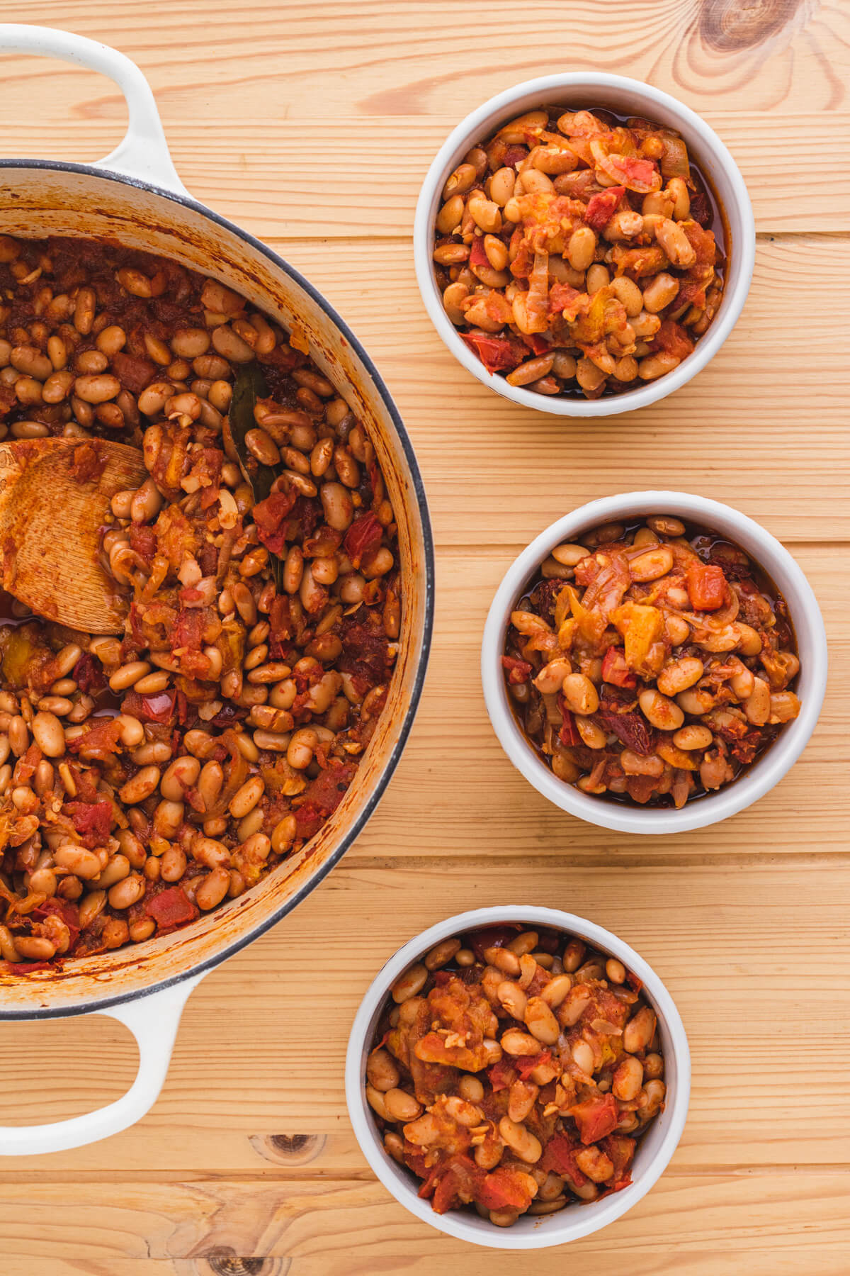 A Dutch oven and three bowls filled with chipotle pinto beans with peaches and tomatoes.