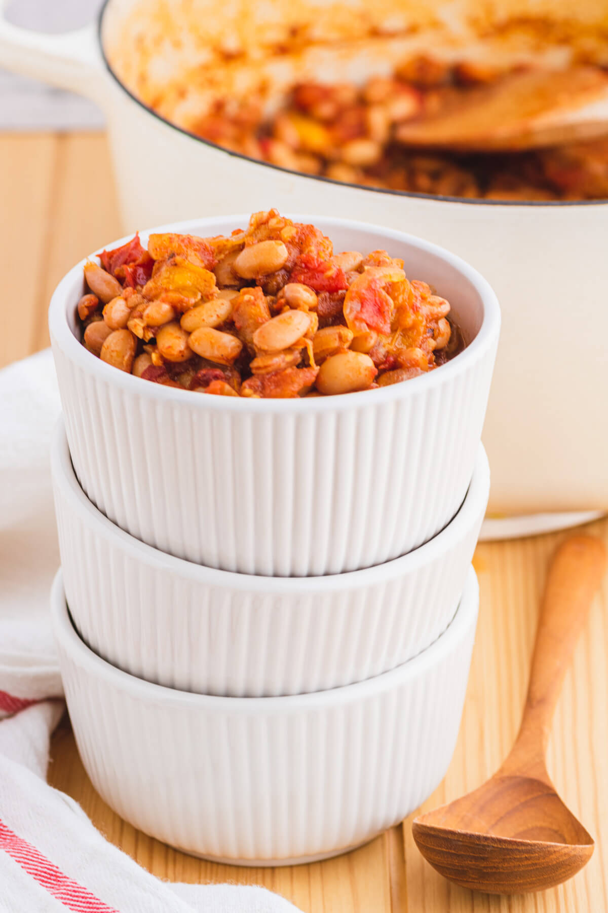 A bowl of chipotle pinto beans with peaches and tomatoes on top of a stack of bowls.