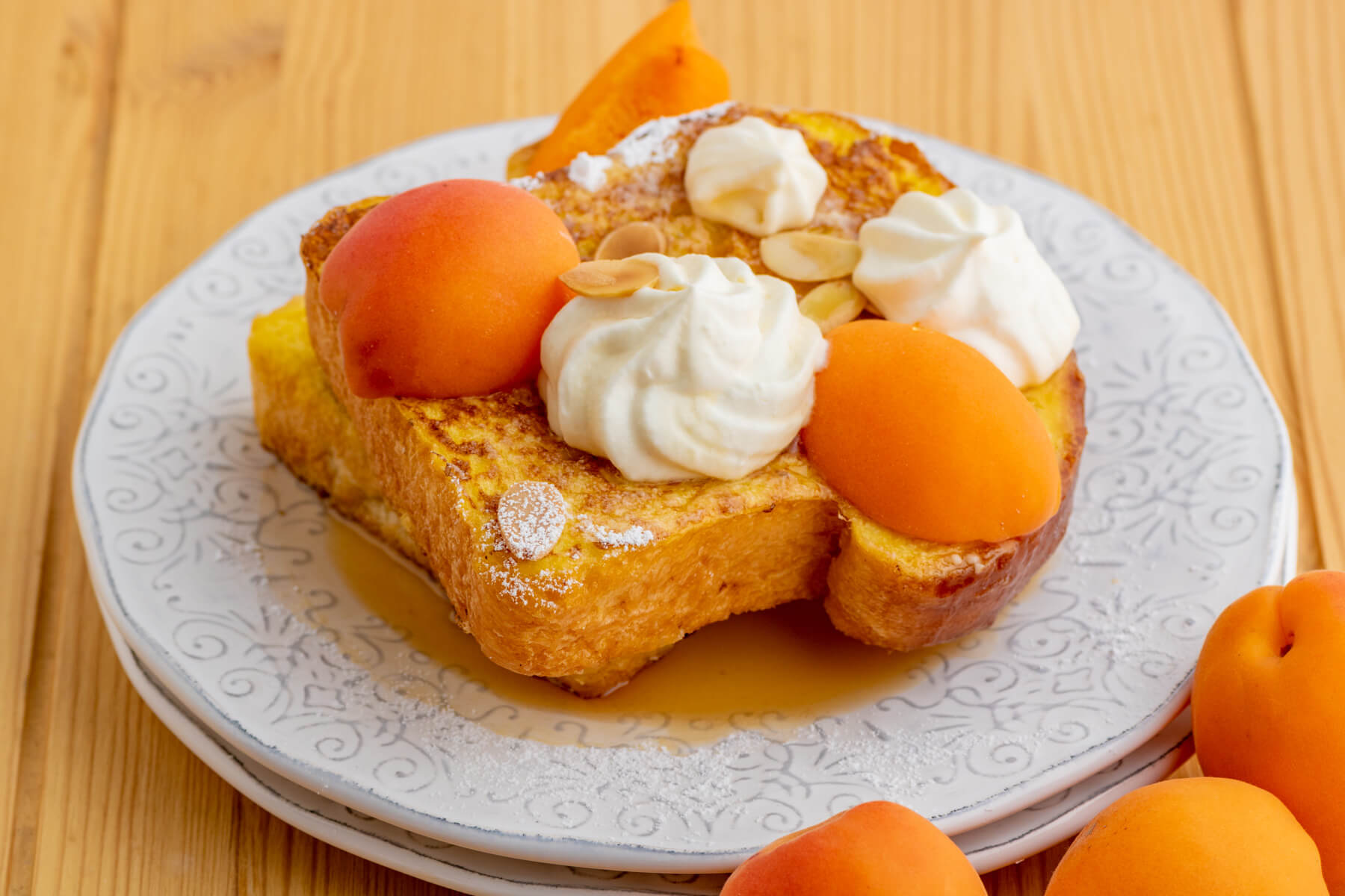Two slices of golden Brioche French toast with whipped mascarpone cheese and fresh apricot slices on a white plate.