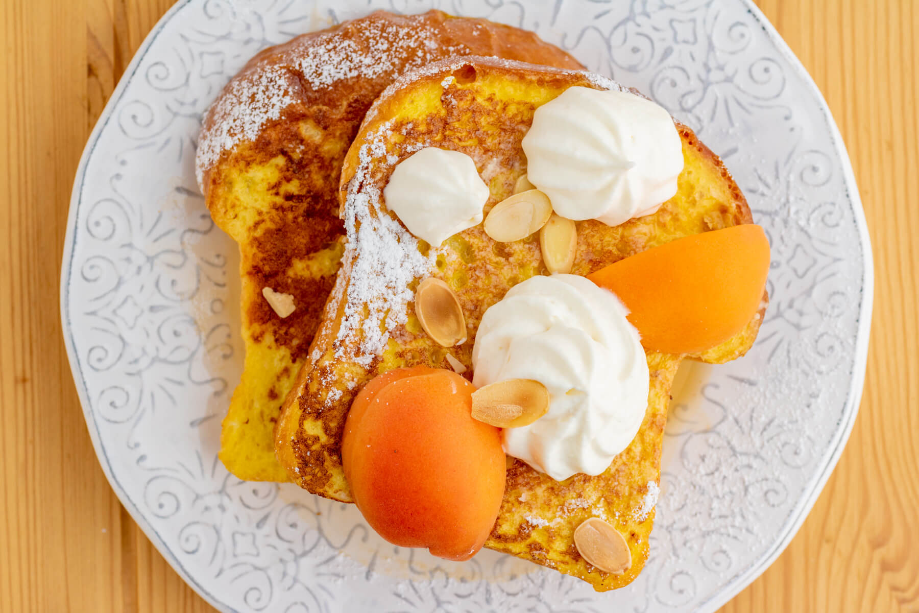 Two slices of golden Brioche French toast with whipped mascarpone cheese and fresh apricot slices on a white plate.