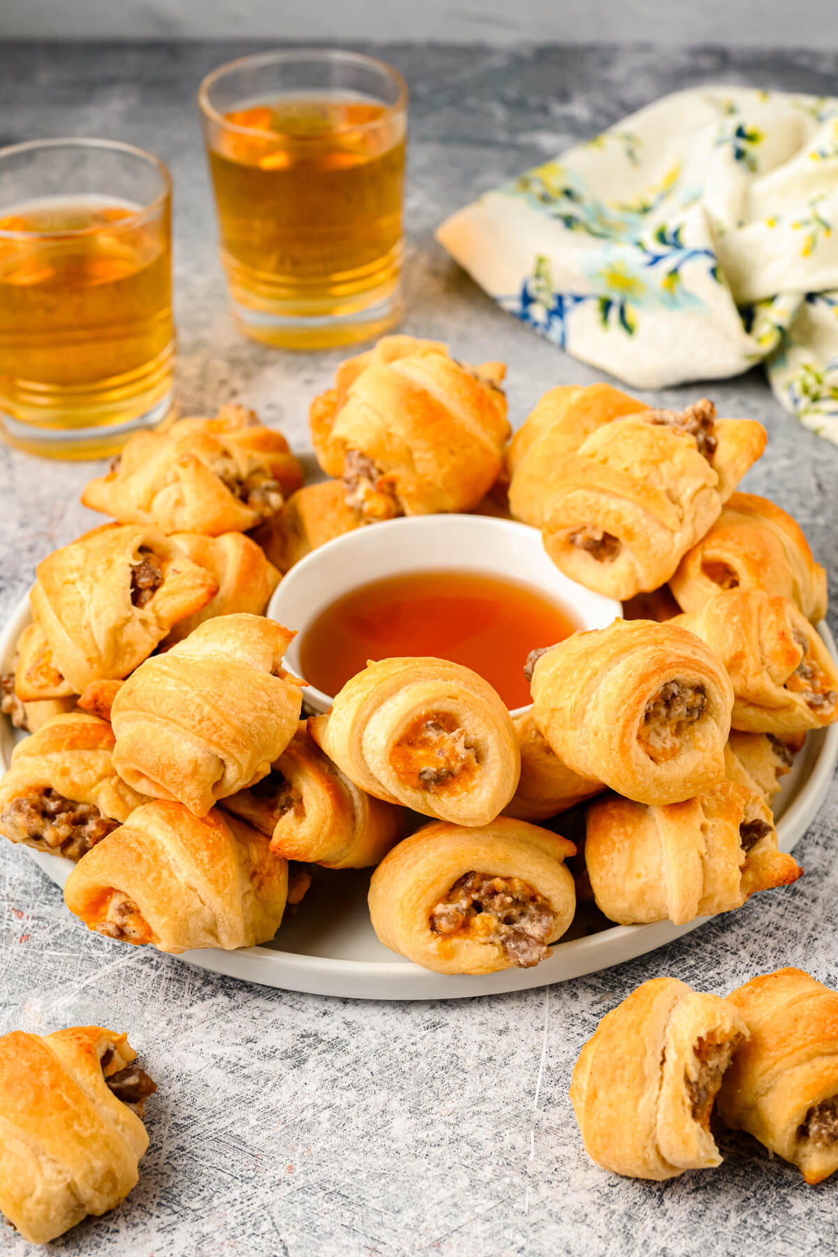A platter of golden baked Sausage Cream Cheese Crescent Rolls surrounding a bowl of dipping sauce.