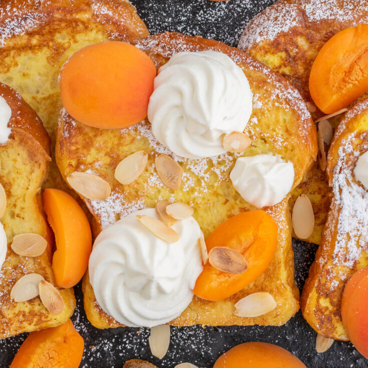 A black tray containing slices of golden Brioche French toast with whipped mascarpone cheese and fresh apricot slices.