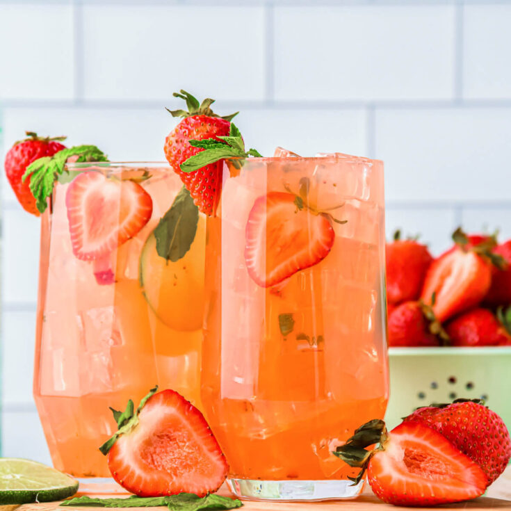Two tall cocktail glasses filled with Strawberry Mojito cocktail and garnished with strawberries, lime, and mint.