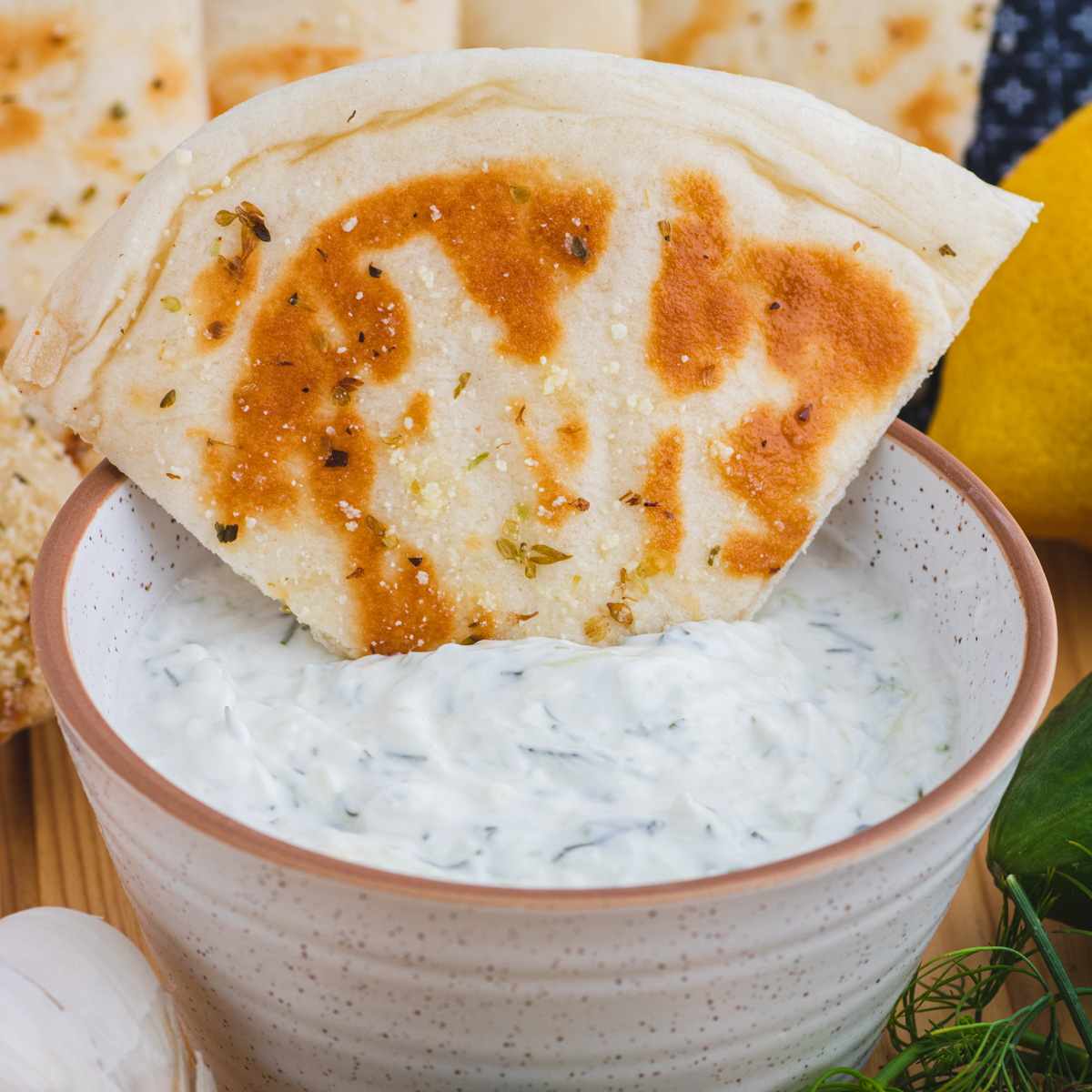 A toasted triangle of pita bread in a bowl of creamy tzatziki sauce.