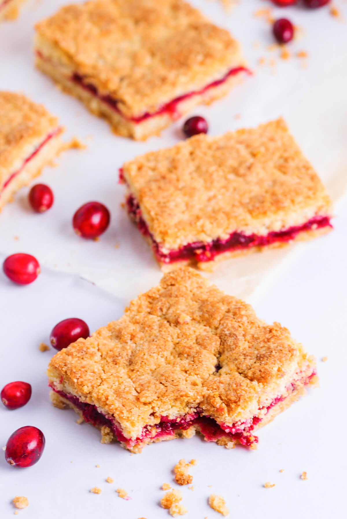 Three squares of Cranberry Bars on a white background with fresh cranberries.