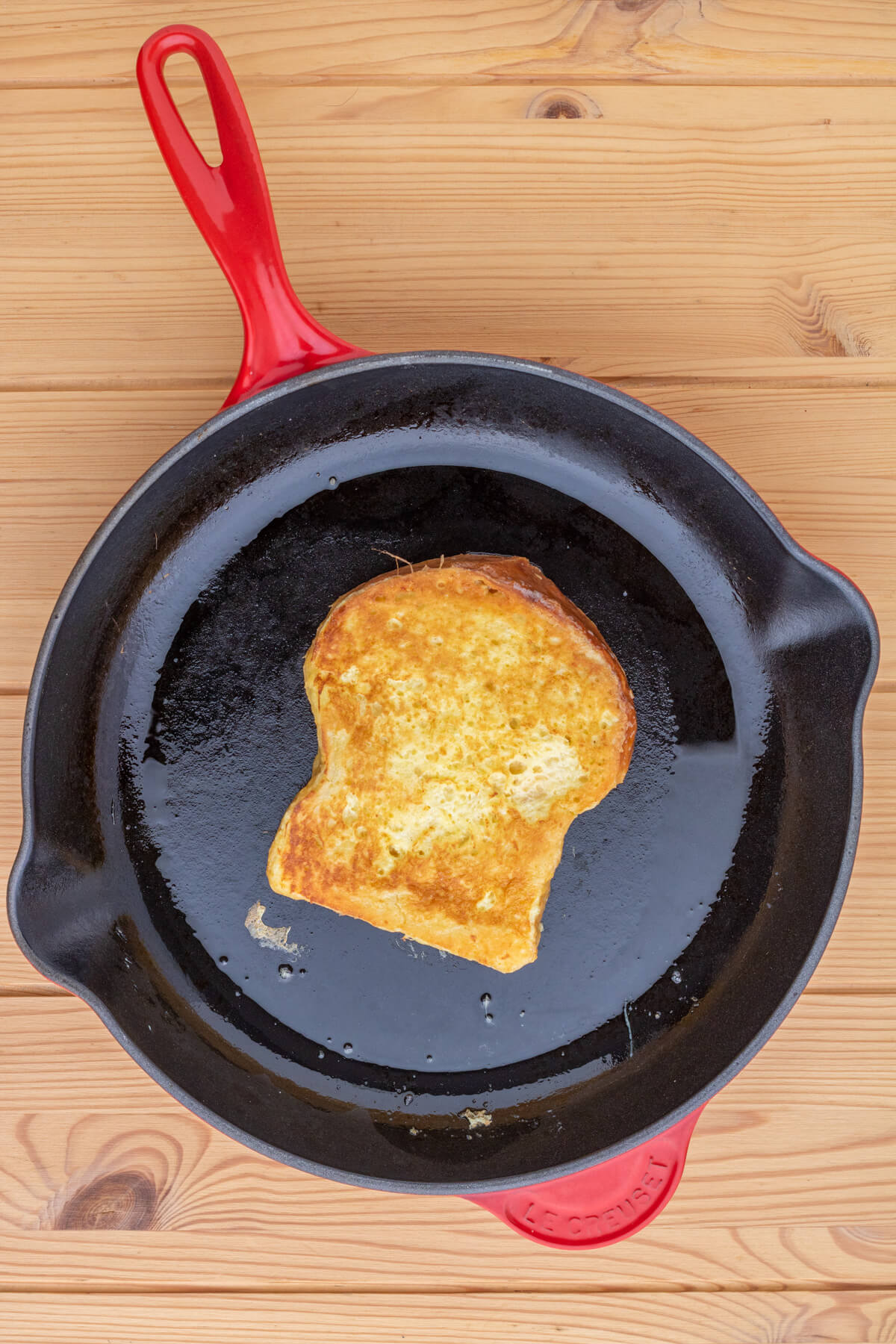 A slice of golden Brioche French toast in a red le creuset frying pan.