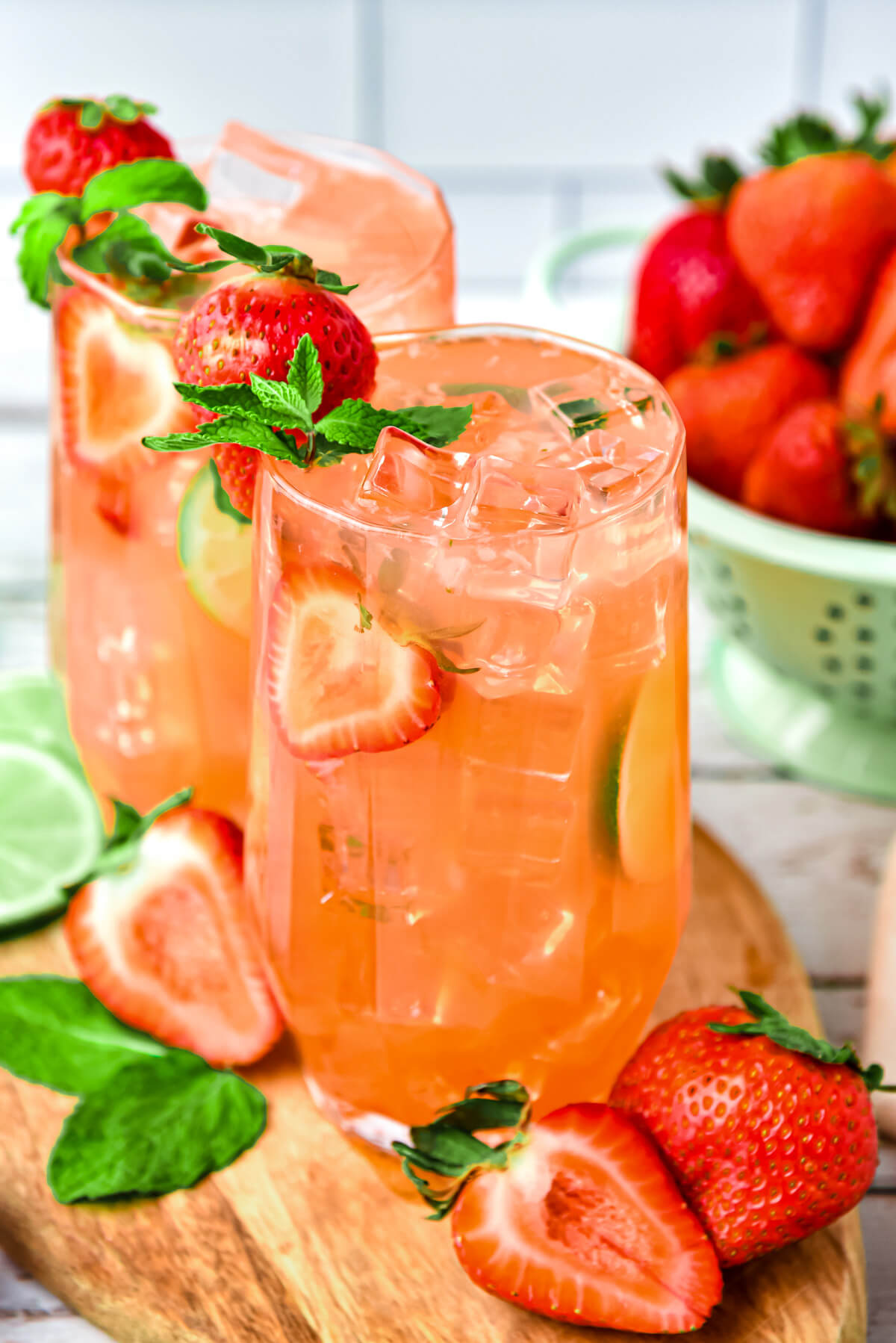 Two tall cocktail glasses filled with Strawberry Mojito cocktail and garnished with strawberries, lime, and mint.