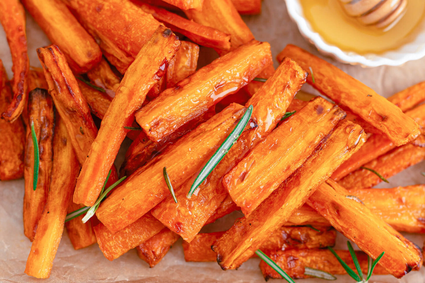 Perfectly roasted air fryer carrots on a parchment lined tray with rosemary and a small dish of honey.