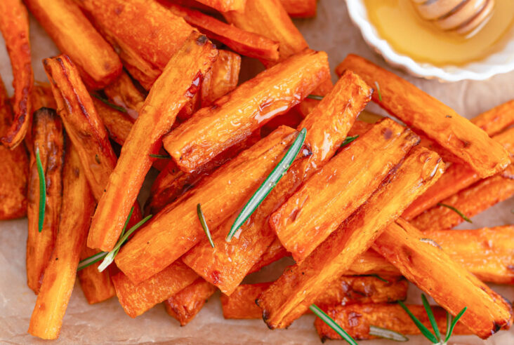 Perfectly roasted air fryer carrots on a parchment lined tray with rosemary and a small dish of honey.