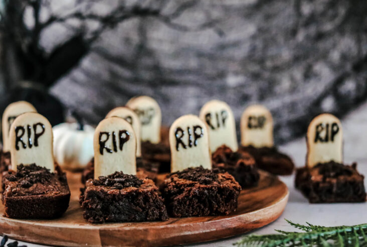 Graveyard Halloween Brownies decorated with tombstones and oreo dirt in a graveyard setting.