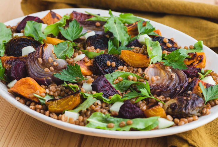 A white serving platter filled with a colourful Harvest Salad featuring roasted beets, onions, Brussels sprouts, and wheat berries.