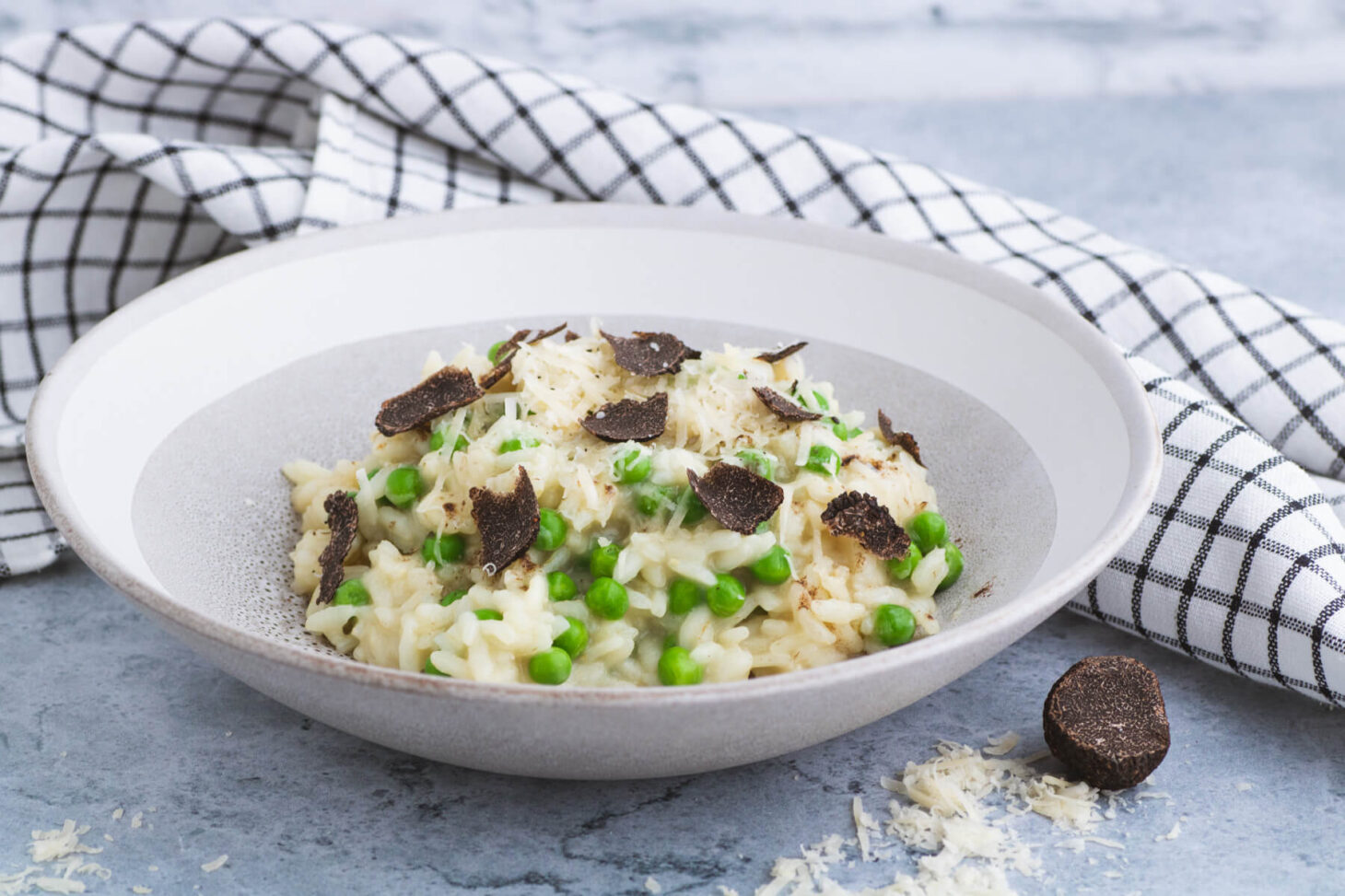 A stone bowl containing creamy truffle risotto studded with green peas and sliced winter truffle.
