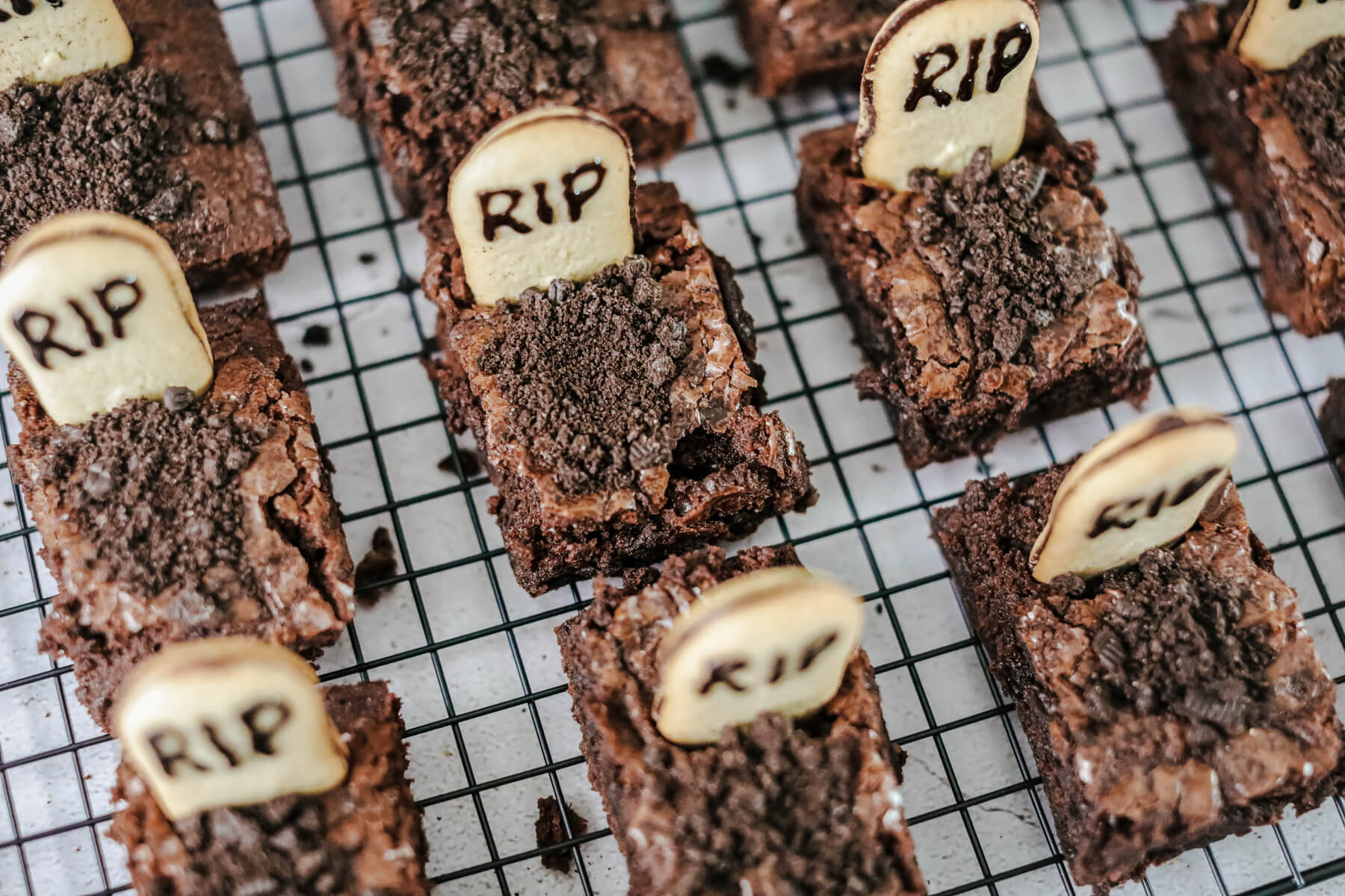 Graveyard Halloween Brownies decorated with tombstones and oreo dirt on a wire cooling rack.