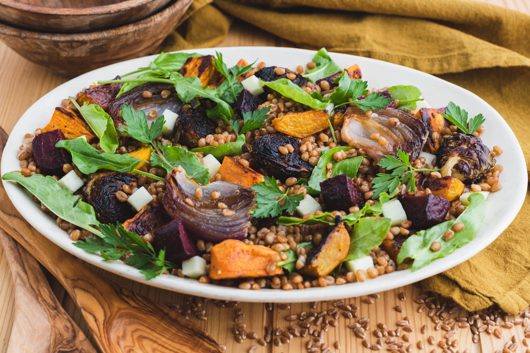 A white serving platter filled with a colourful Harvest Salad featuring roasted beets, onions, Brussels sprouts, and wheat berries.
