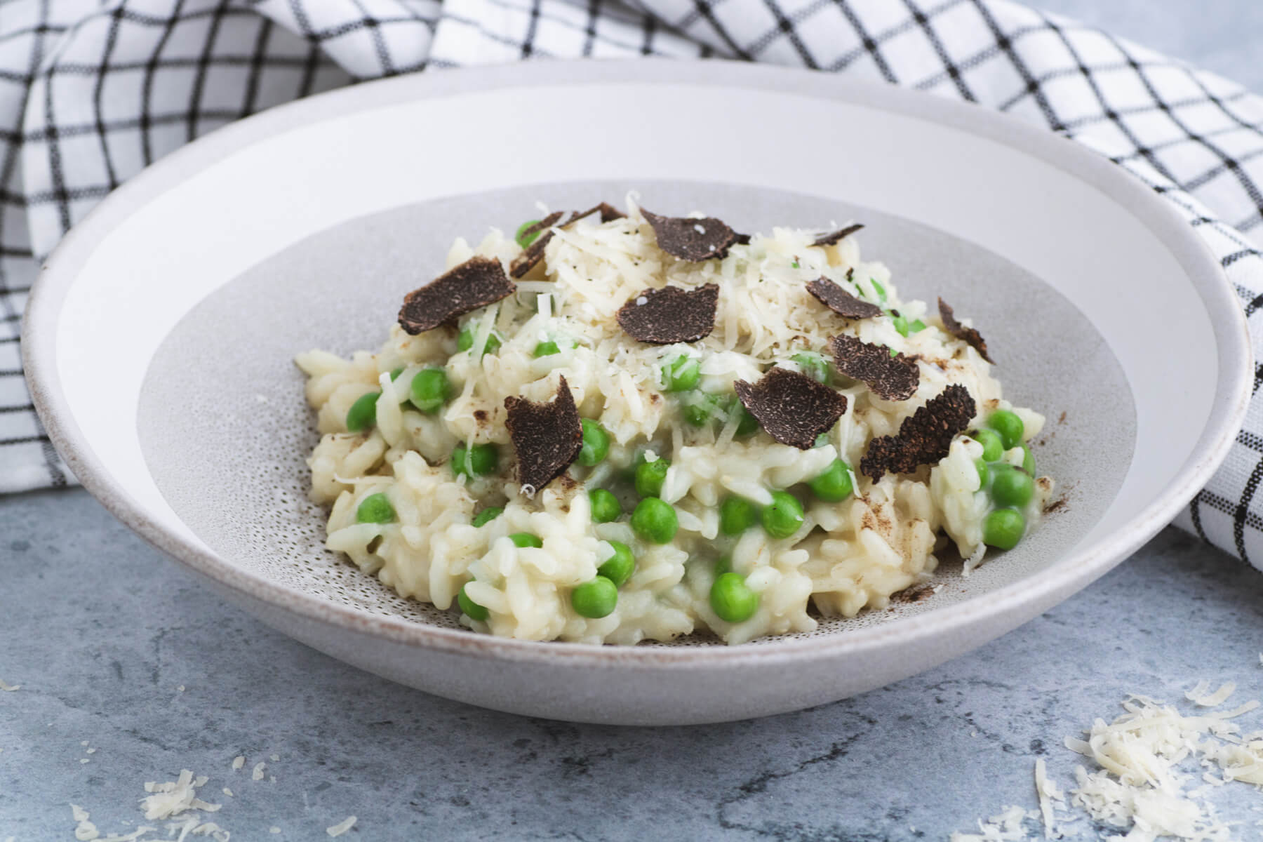 A stone bowl containing creamy truffle risotto studded with green peas and sliced winter truffle.