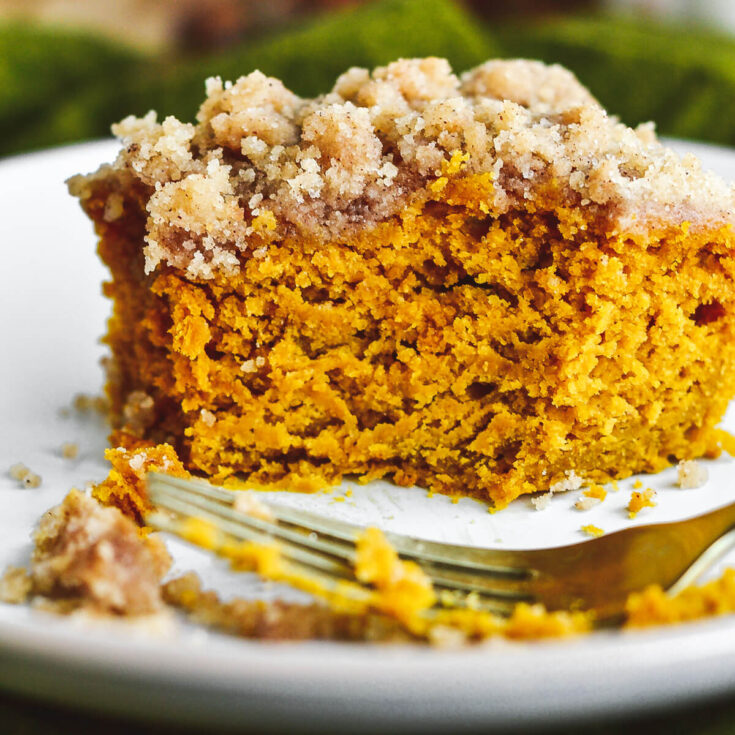 A square of fluffy orange pumpkin coffee cake topped with streusel on a plate with a bite taken out of it.